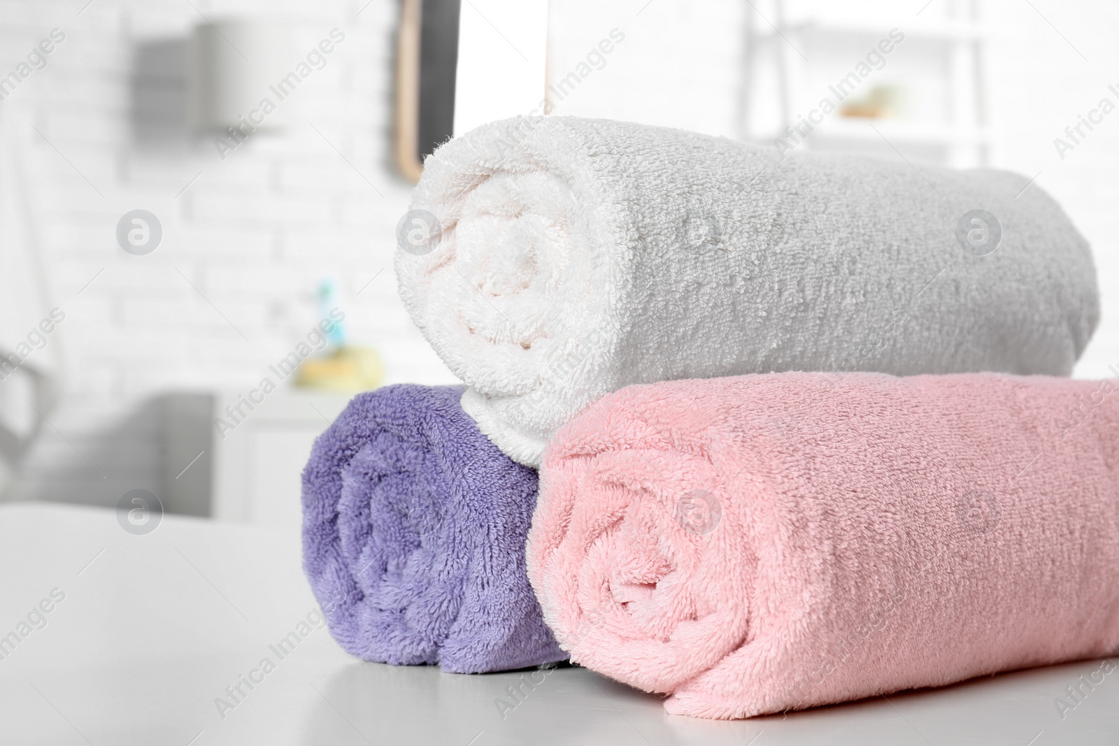 Photo of Rolled fresh towels on table in bathroom, closeup. Space for text