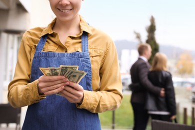 Photo of Happy waitress holding tips in outdoor cafe, closeup. Space for text