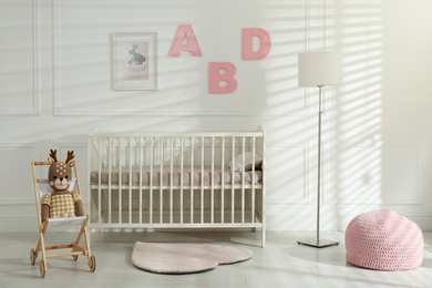 Photo of Comfortable crib near wall with pink letters in baby room. Interior design