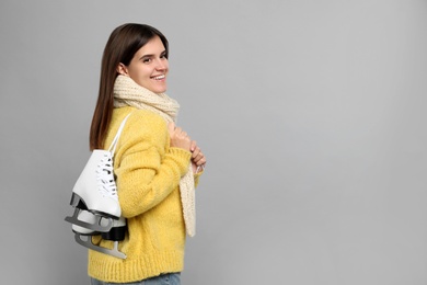 Happy woman with ice skates on grey background. Space for text