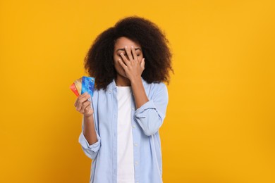 Photo of Confused woman with credit cards on orange background. Debt problem