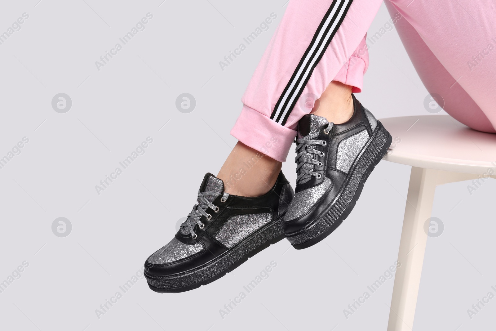 Photo of Woman in stylish sport shoes sitting on stool against light background