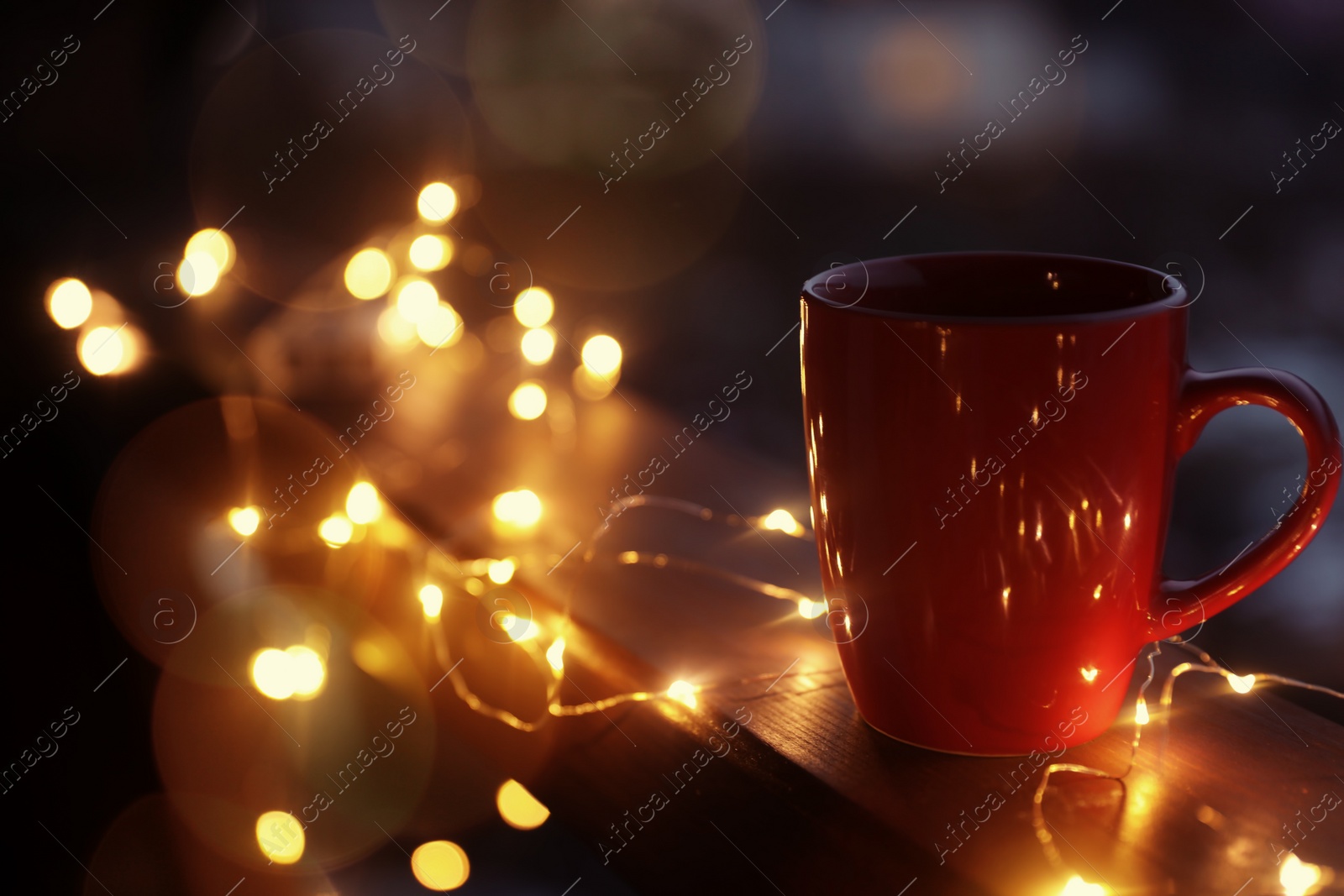 Photo of Cup of hot beverage on balcony railing decorated with Christmas lights, space for text. Winter evening