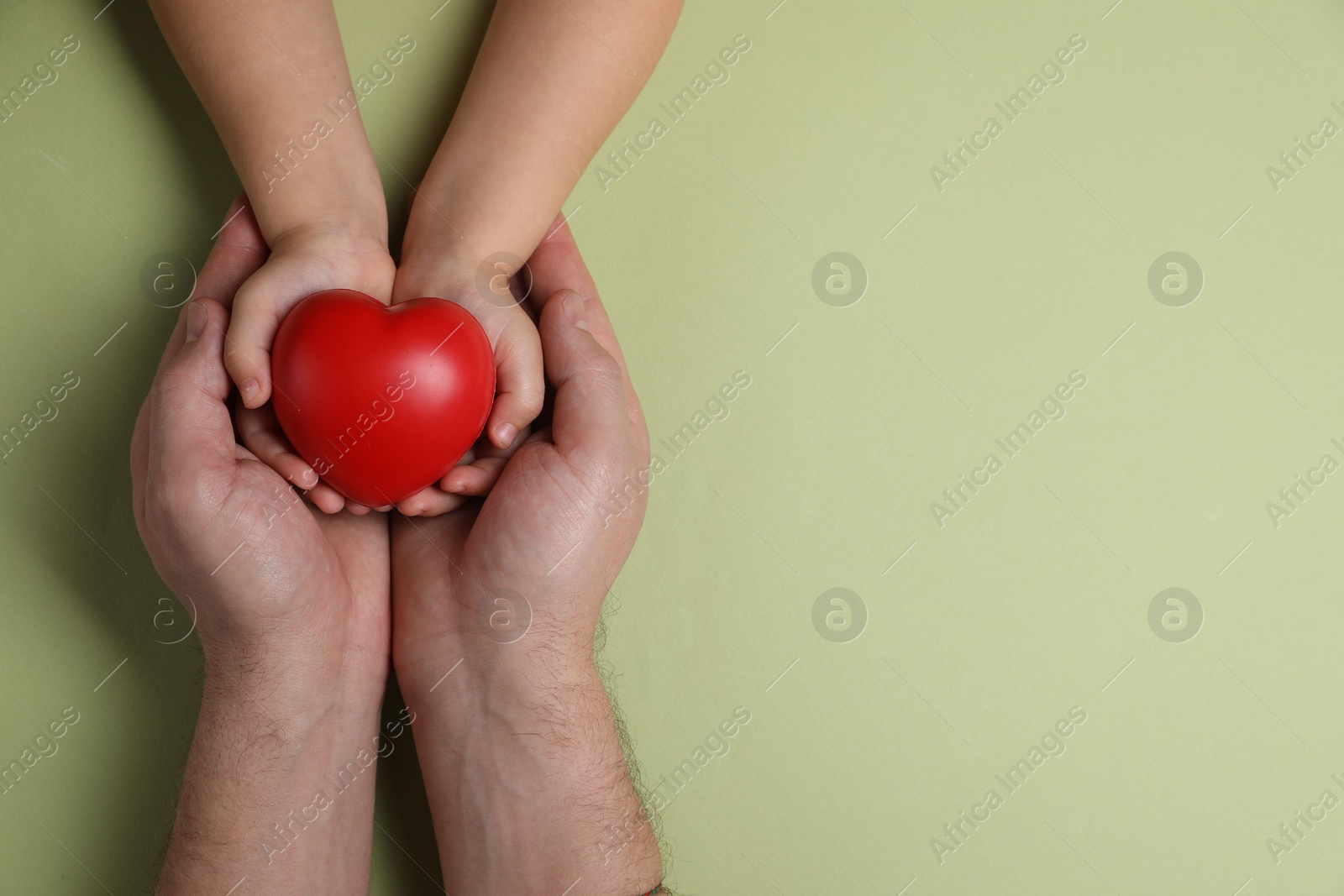 Photo of Father and his child holding red decorative heart on light green background, top view. Space for text