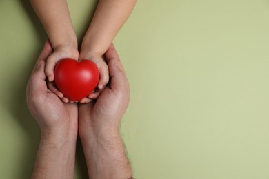 Father and his child holding red decorative heart on light green background, top view. Space for text