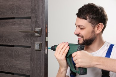Photo of Worker with screw gun repairing door lock indoors