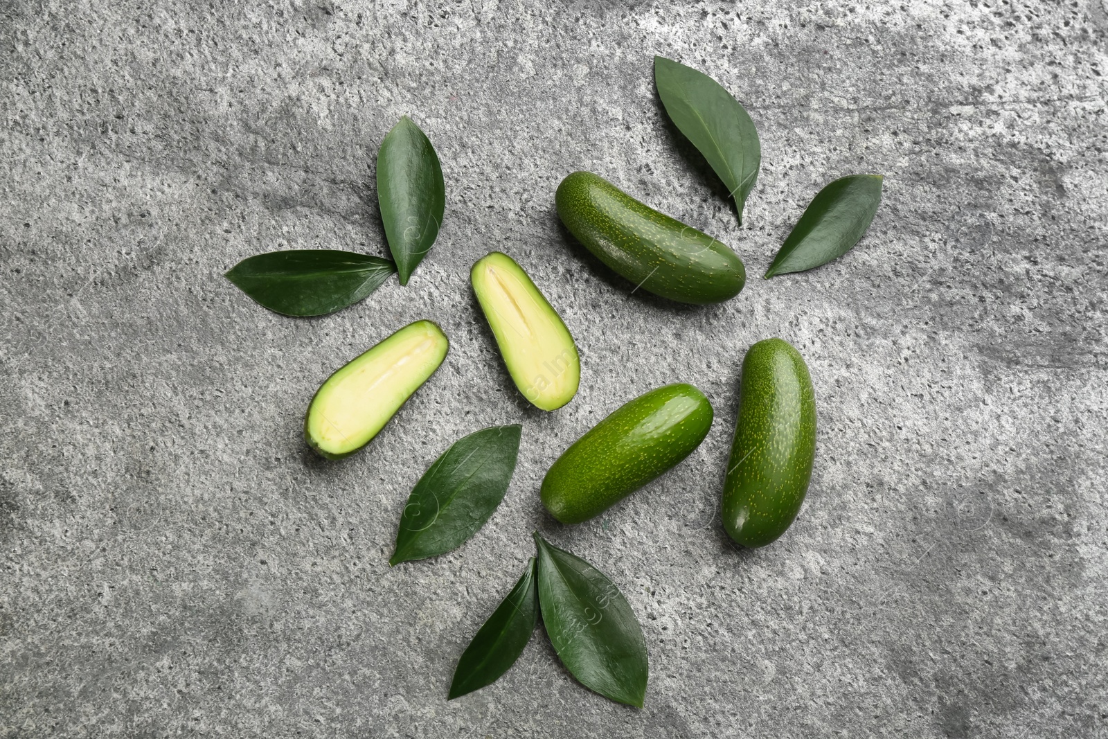 Photo of Fresh seedless avocados with green leaves on grey table, flat lay