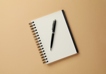 Notebook and pen on beige background, top view