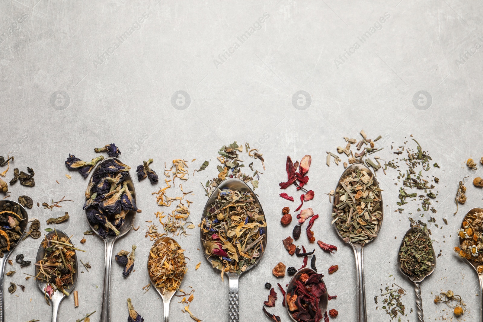 Photo of Flat lay composition with different dry teas and spoons on light table. Space for text