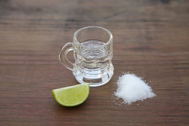Photo of Mexican tequila shot with lime slice and salt on wooden table, closeup. Drink made from agave