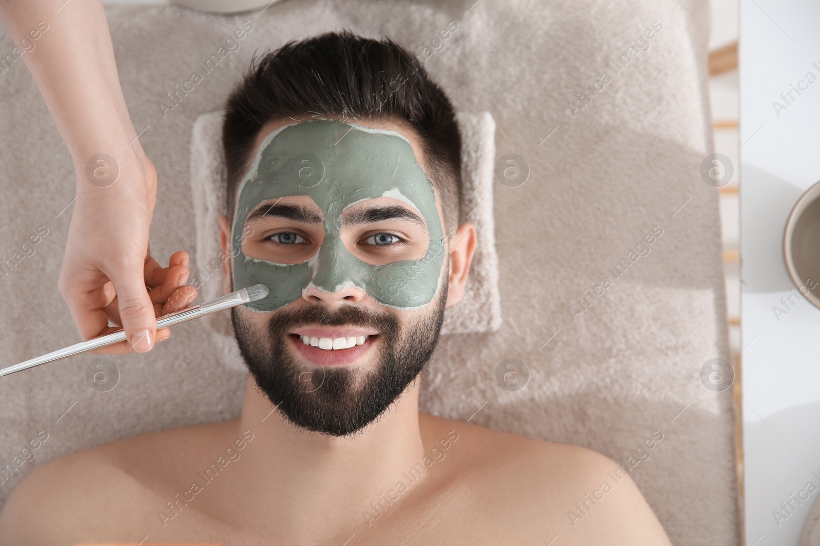 Photo of Cosmetologist applying mask on man's face in spa salon, top view