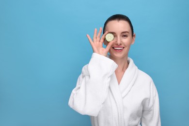 Photo of Beautiful woman covering eye with piece of cucumber on light blue background, space for text