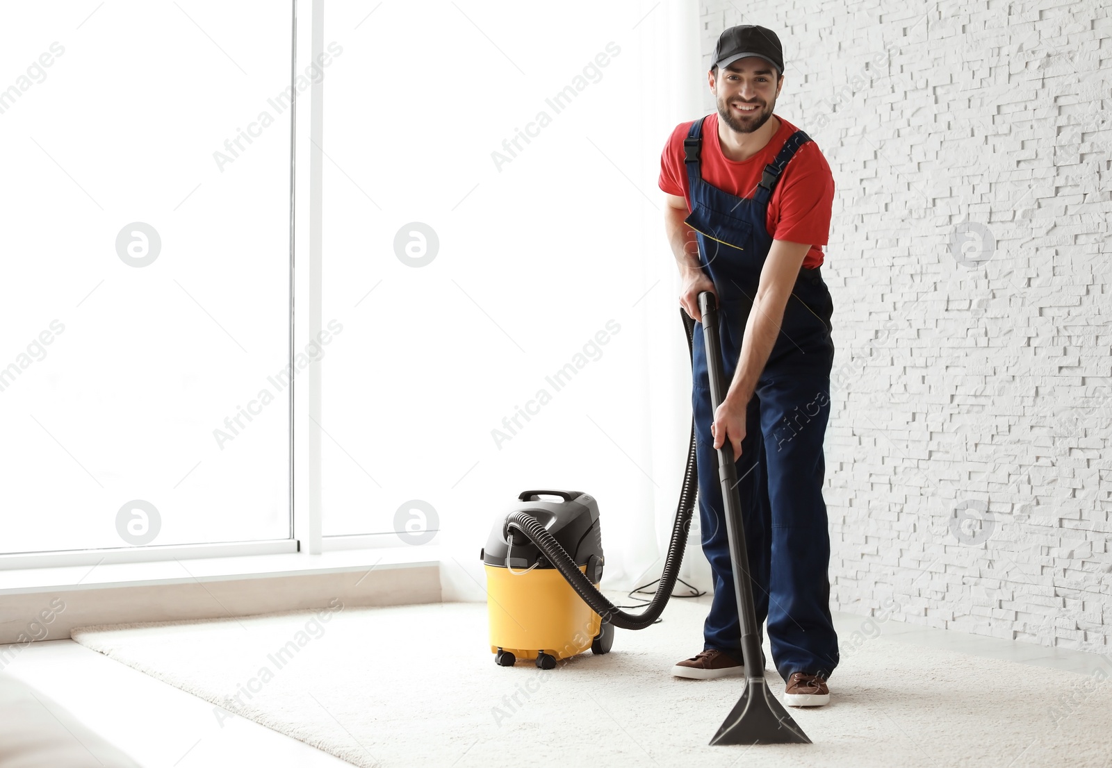 Photo of Male worker cleaning carpet with vacuum indoors