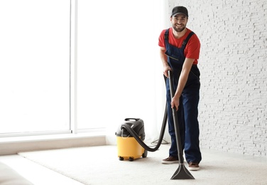 Male worker cleaning carpet with vacuum indoors