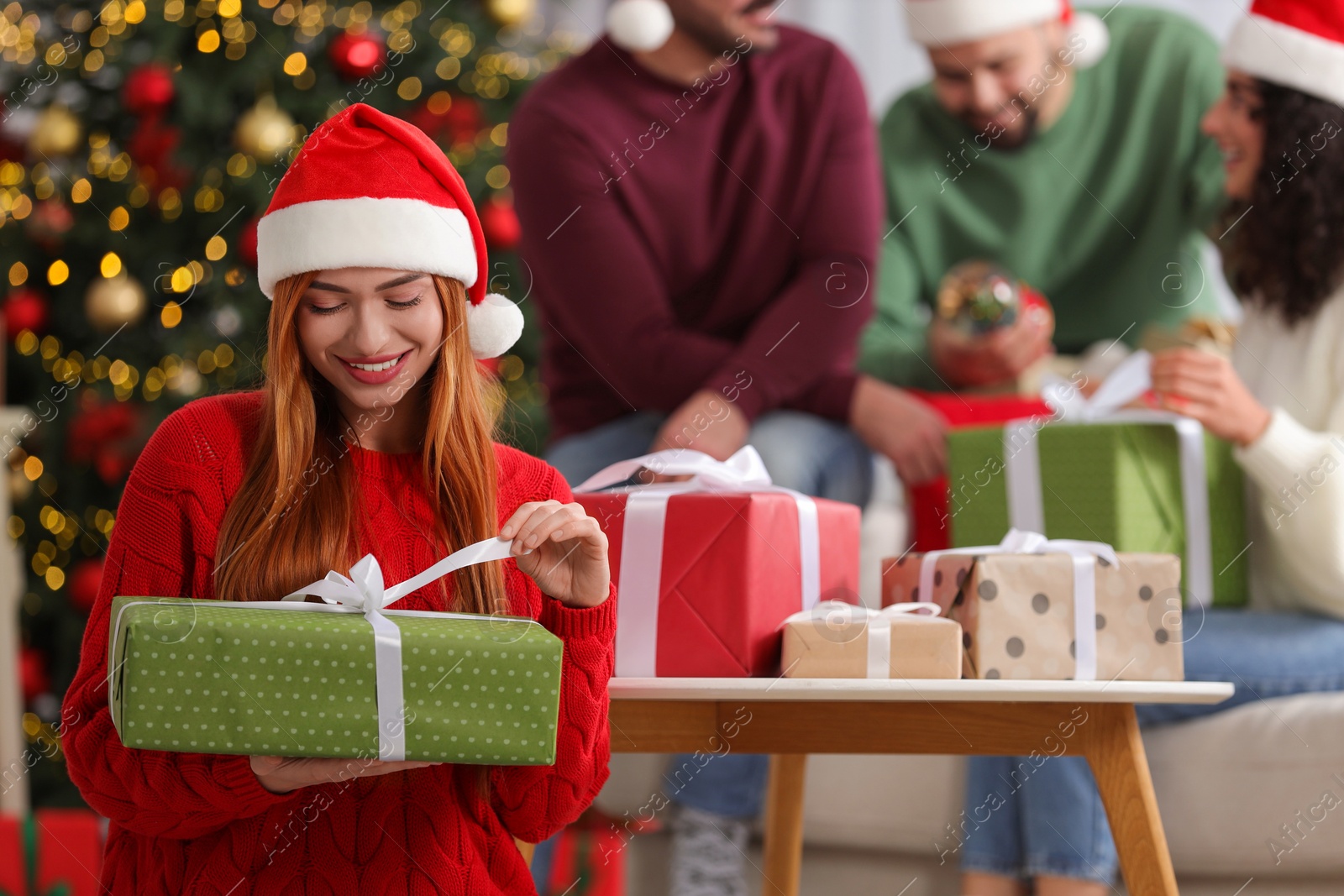 Photo of Christmas celebration in circle of friends. Happy young woman opening gift at home, selective focus