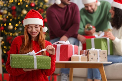 Christmas celebration in circle of friends. Happy young woman opening gift at home, selective focus