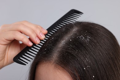 Woman with comb examining her hair and scalp on grey background, closeup. Dandruff problem