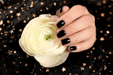 Photo of Woman with black manicure holding beautiful flower on dark background, closeup. Nail polish trends
