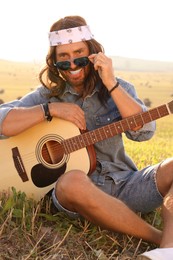 Photo of Portrait of happy hippie man with guitar in field