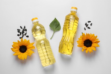 Bottles of cooking oil, sunflowers and seeds on white table, flat lay