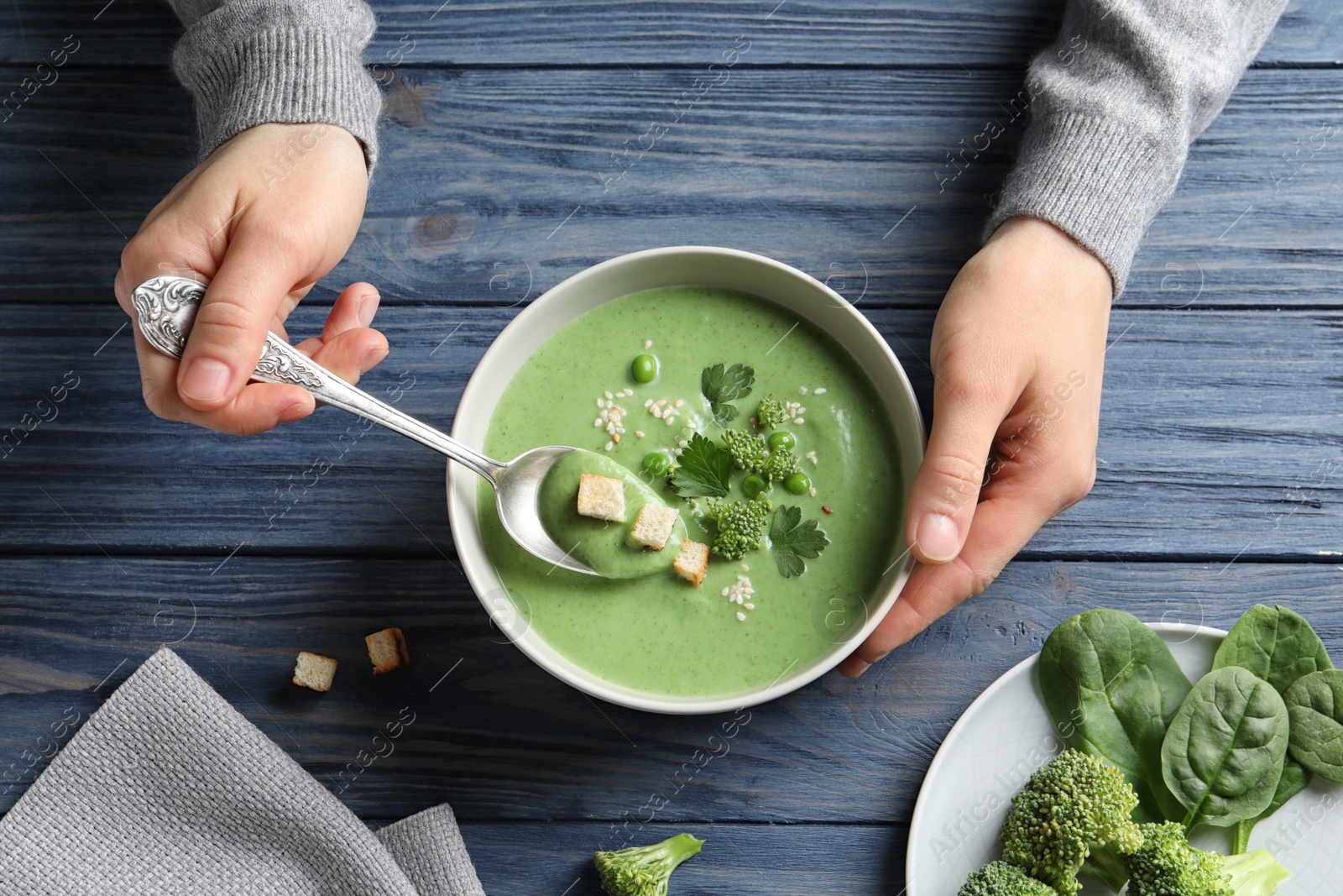 Photo of Woman eating fresh vegetable detox soup made of broccoli and green peas with croutons at table, top view