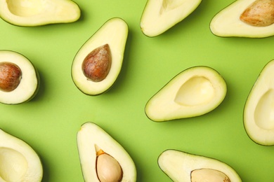 Cut fresh ripe avocados on green background, flat lay