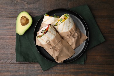 Delicious sandwich wraps with fresh vegetables and avocado on wooden table, top view