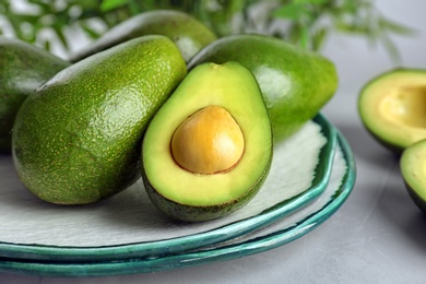 Plate with ripe avocados on grey table