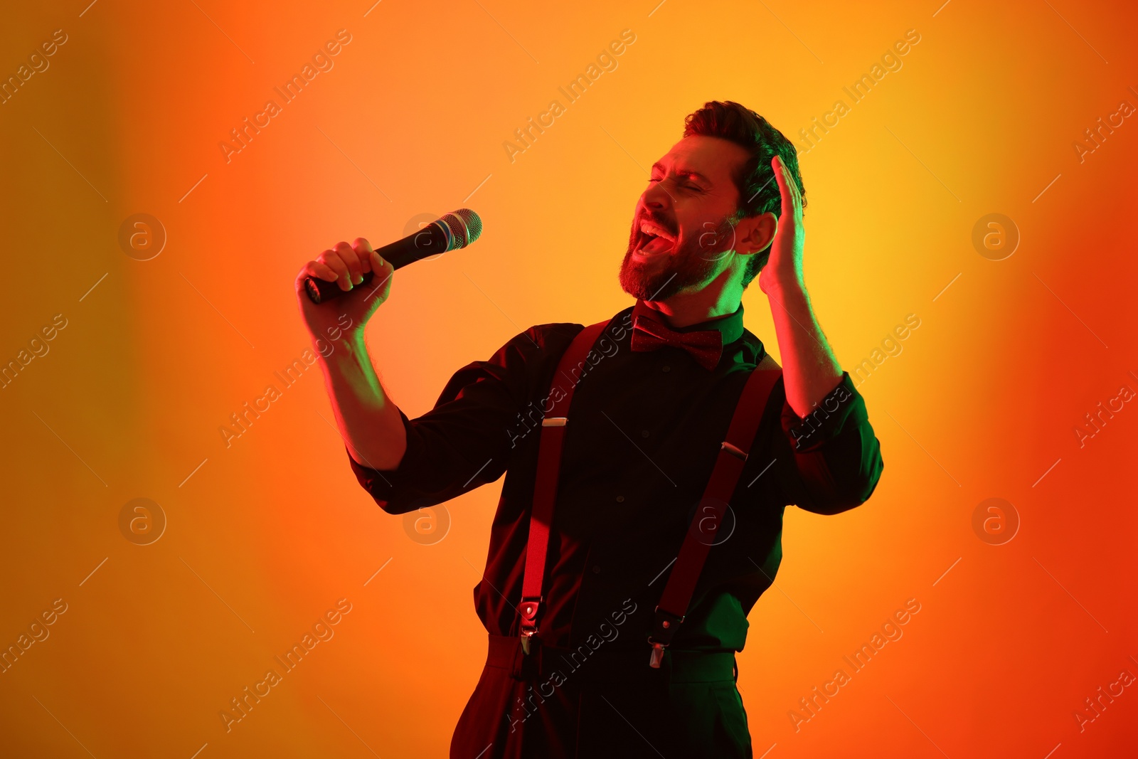 Photo of Emotional man with microphone singing in neon lights on orange background