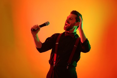 Emotional man with microphone singing in neon lights on orange background