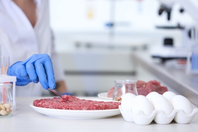Photo of Scientist inspecting forcemeat at table in laboratory, closeup. Food quality control