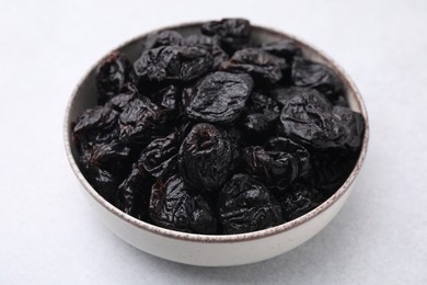 Sweet dried prunes in bowl on light table, closeup