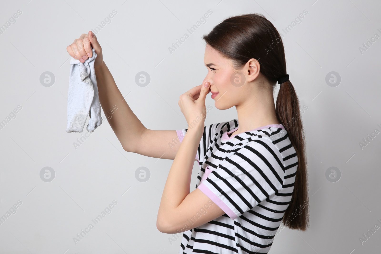 Photo of Young woman feeling bad smell from dirty socks on light grey background