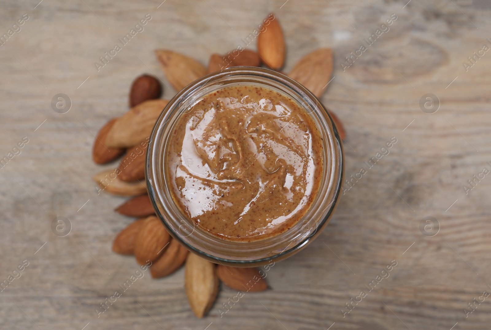 Photo of Tasty almond nut paste in jar on wooden table, top view