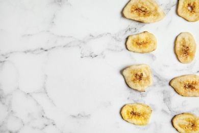 Photo of Flat lay composition with banana slices on marble table, space for text. Dried fruit as healthy snack