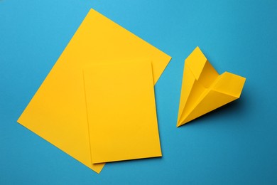 Photo of Handmade yellow plane and pieces of paper on light blue background, flat lay