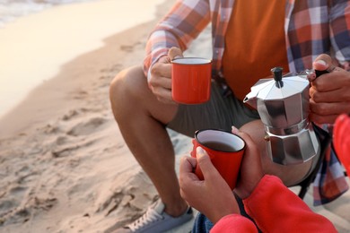 Photo of Couple enjoying hot drink on seashore, closeup. Beach camping