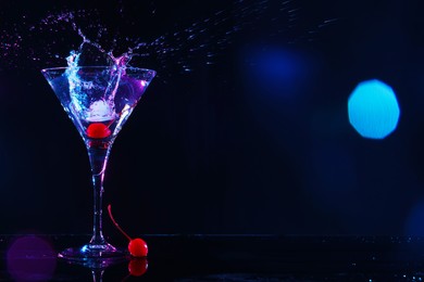 Photo of Martini splashing out of glass and cherry on black background, space for text. Bokeh effect