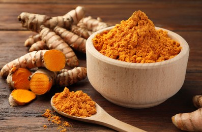 Aromatic turmeric powder and raw roots on wooden table, closeup