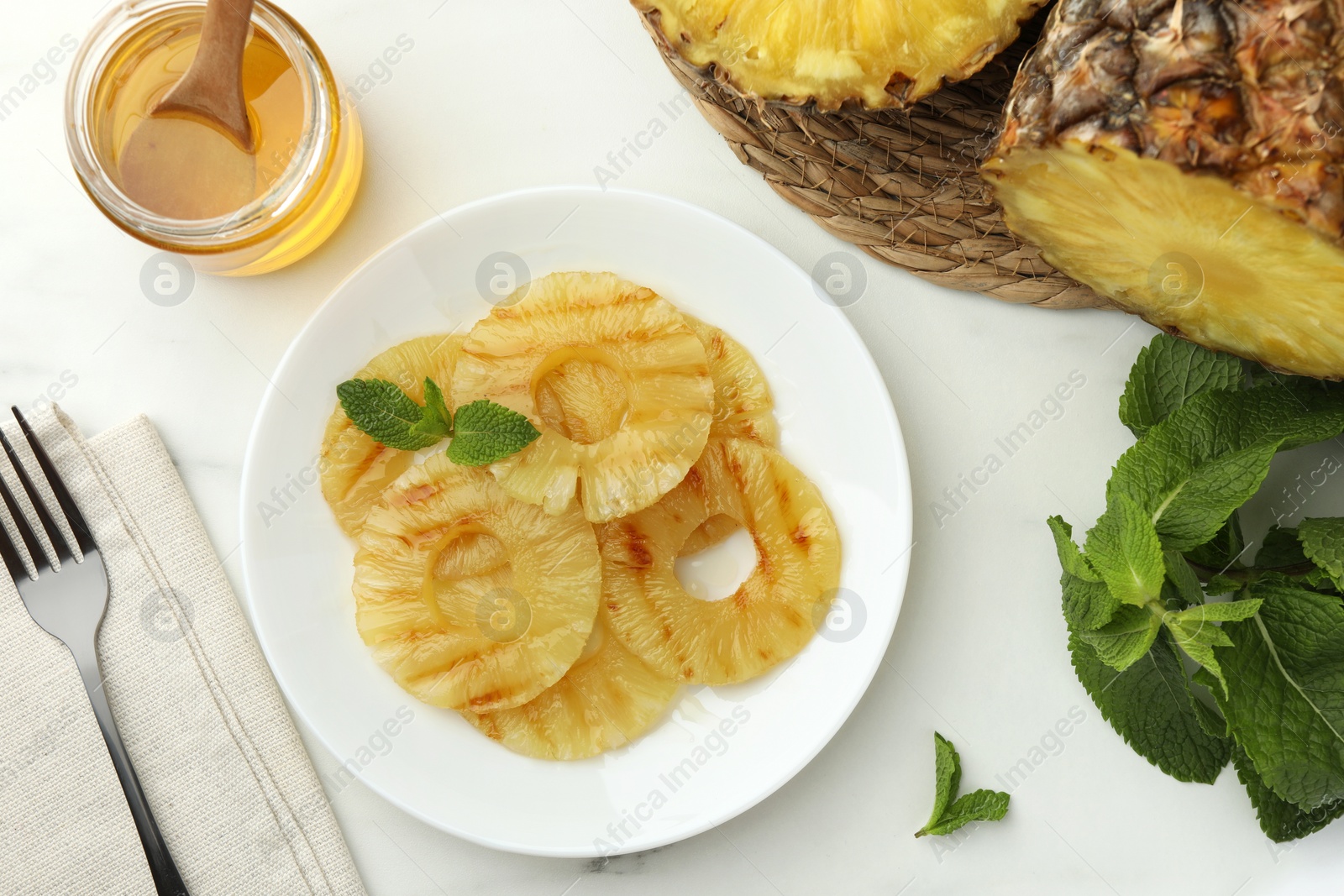 Photo of Tasty grilled pineapple slices served with mint and honey on white table, flat lay