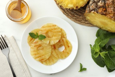 Tasty grilled pineapple slices served with mint and honey on white table, flat lay