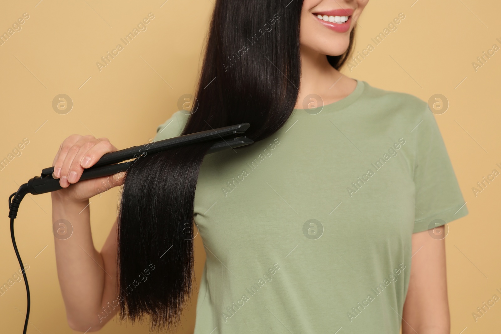 Photo of Happy woman using hair iron on beige background, closeup