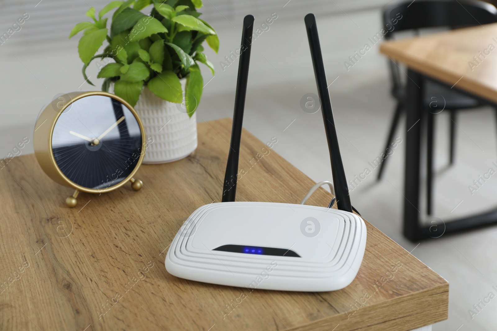 Photo of Wi-Fi router, alarm clock and houseplant on wooden table in room