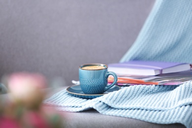 Photo of Cup of coffee, plaid and magazines on sofa