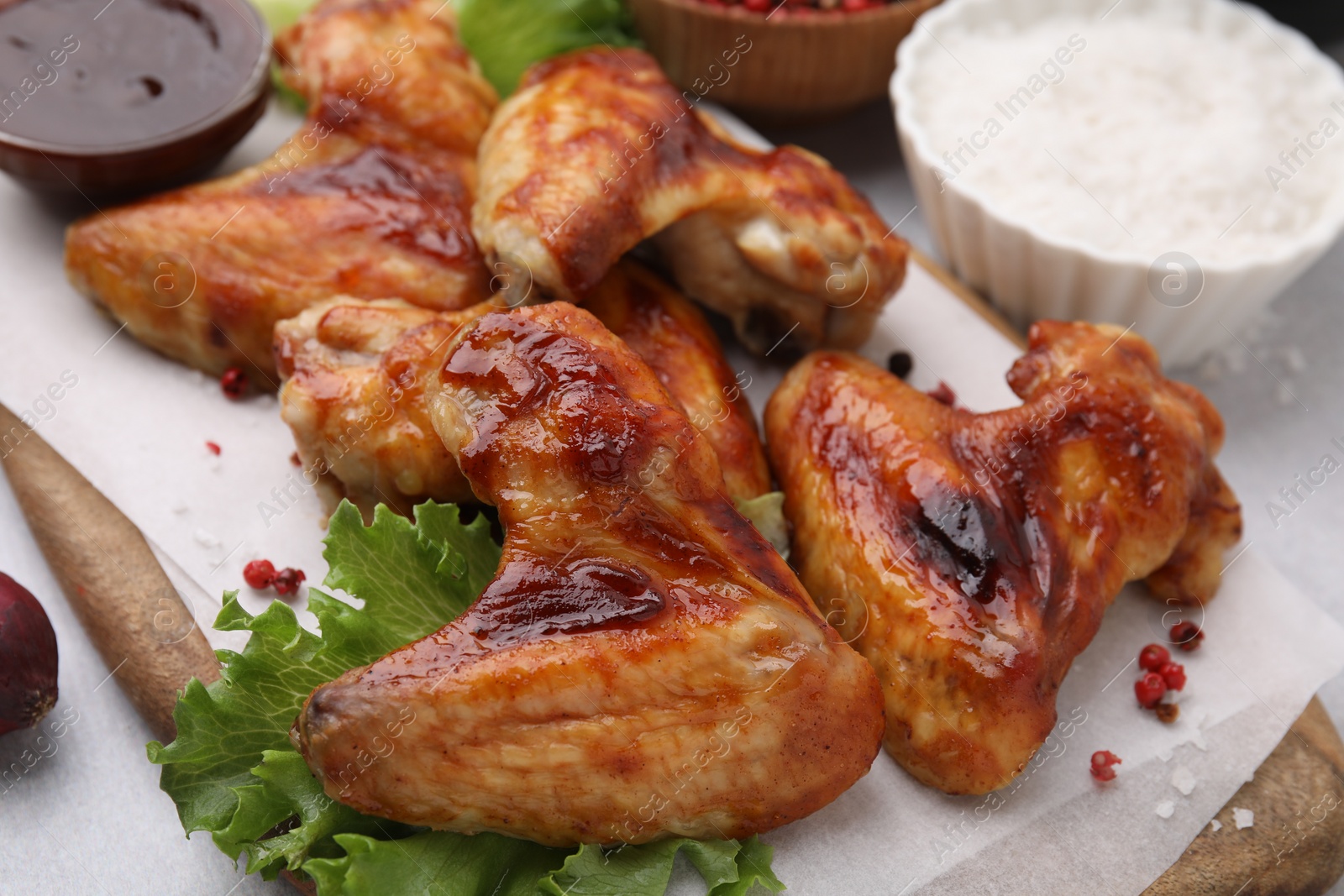 Photo of Fresh marinated chicken wings, spices and lettuce on light table, closeup