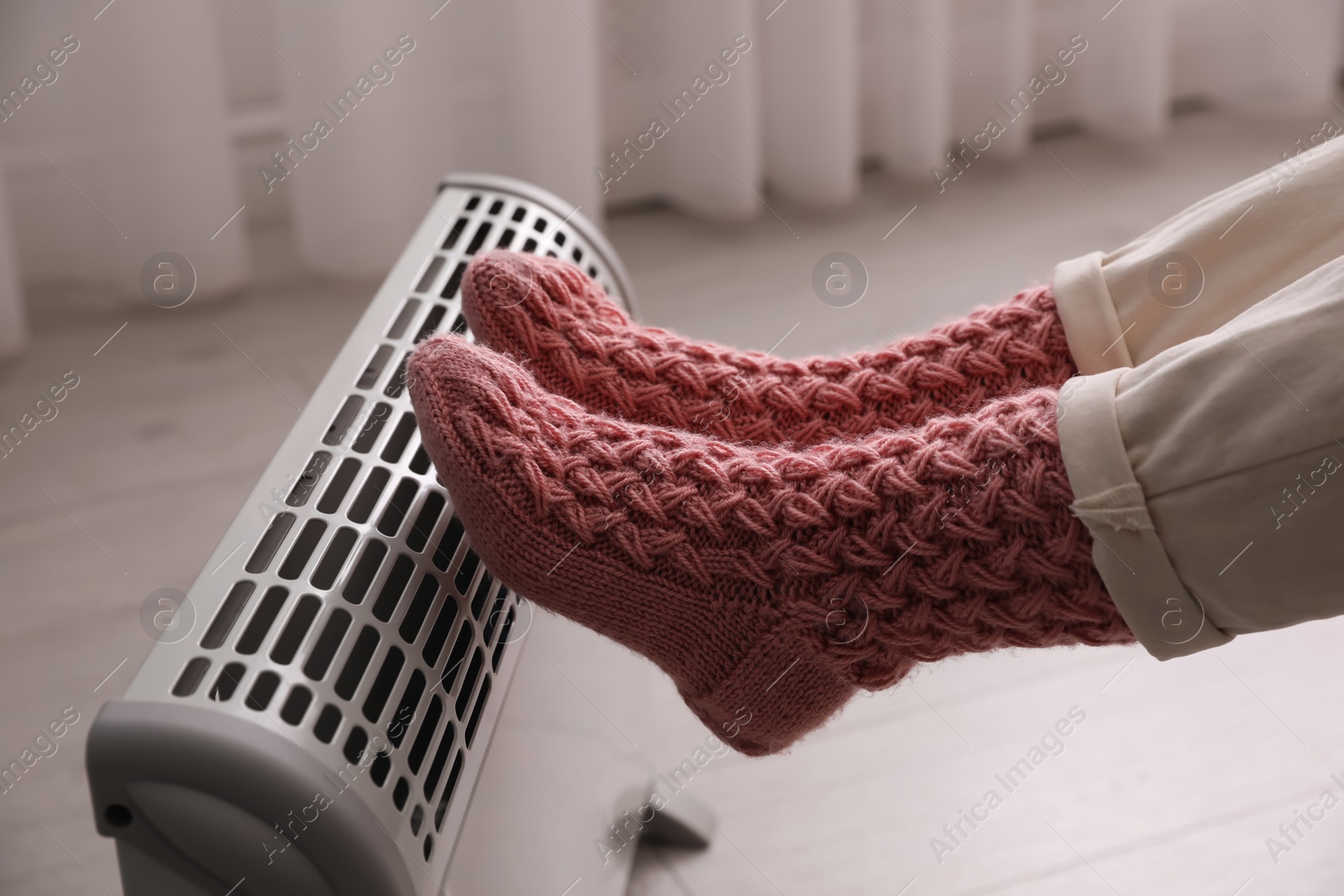 Photo of Woman warming feet on electric heater at home, closeup