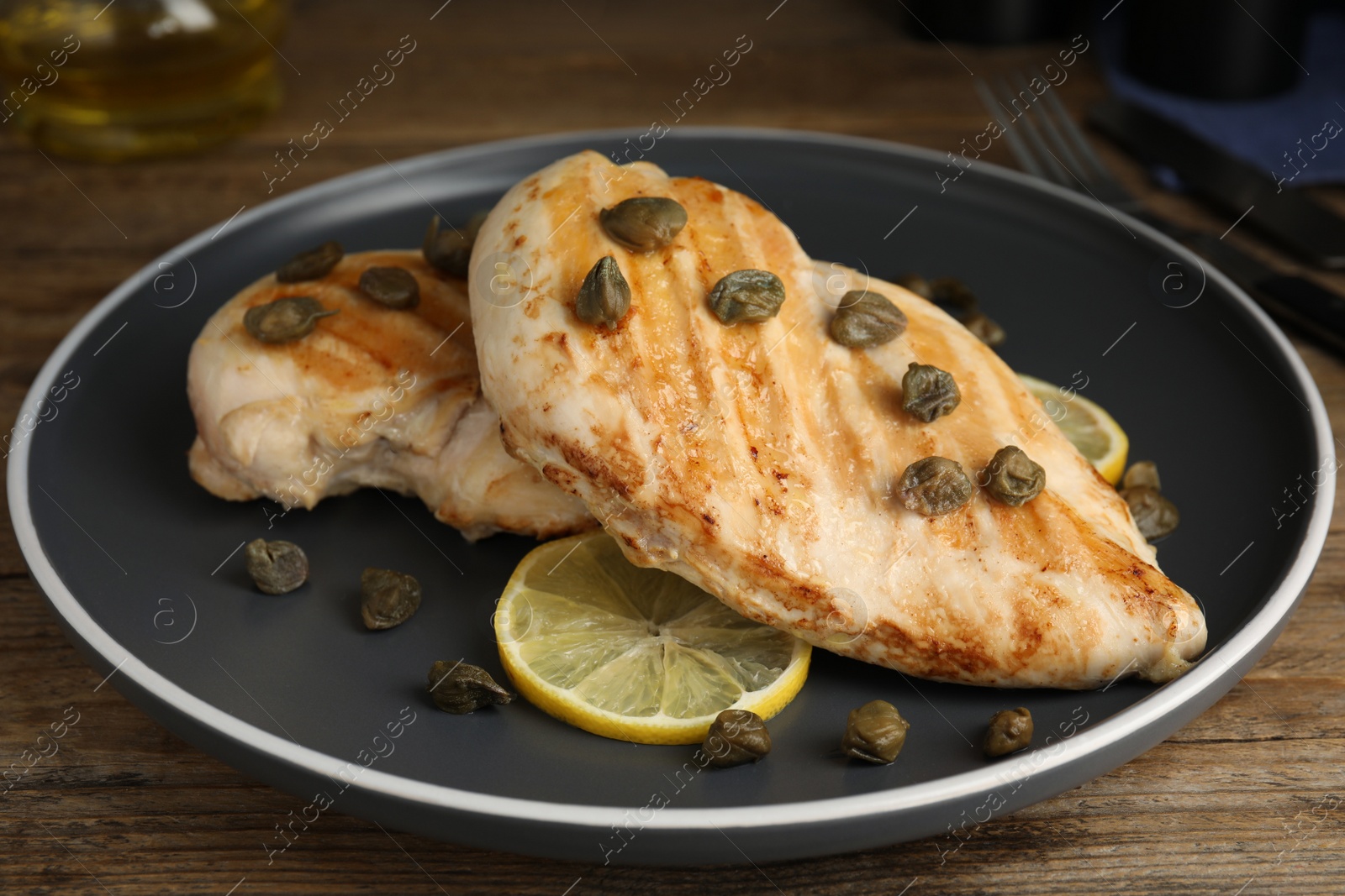 Photo of Delicious chicken fillets with capers and lemon served on wooden table, closeup