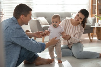 Photo of Parents supporting their baby daughter while she learning to walk at home