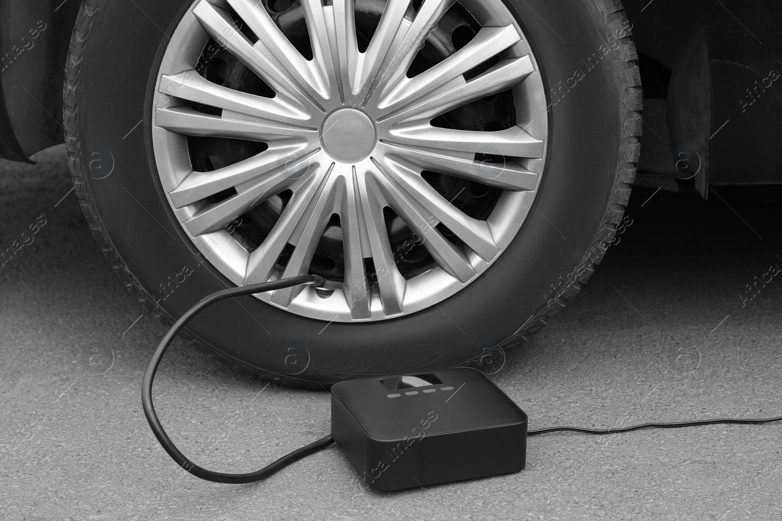 Photo of Inflating car tire with portable air pump outdoors
