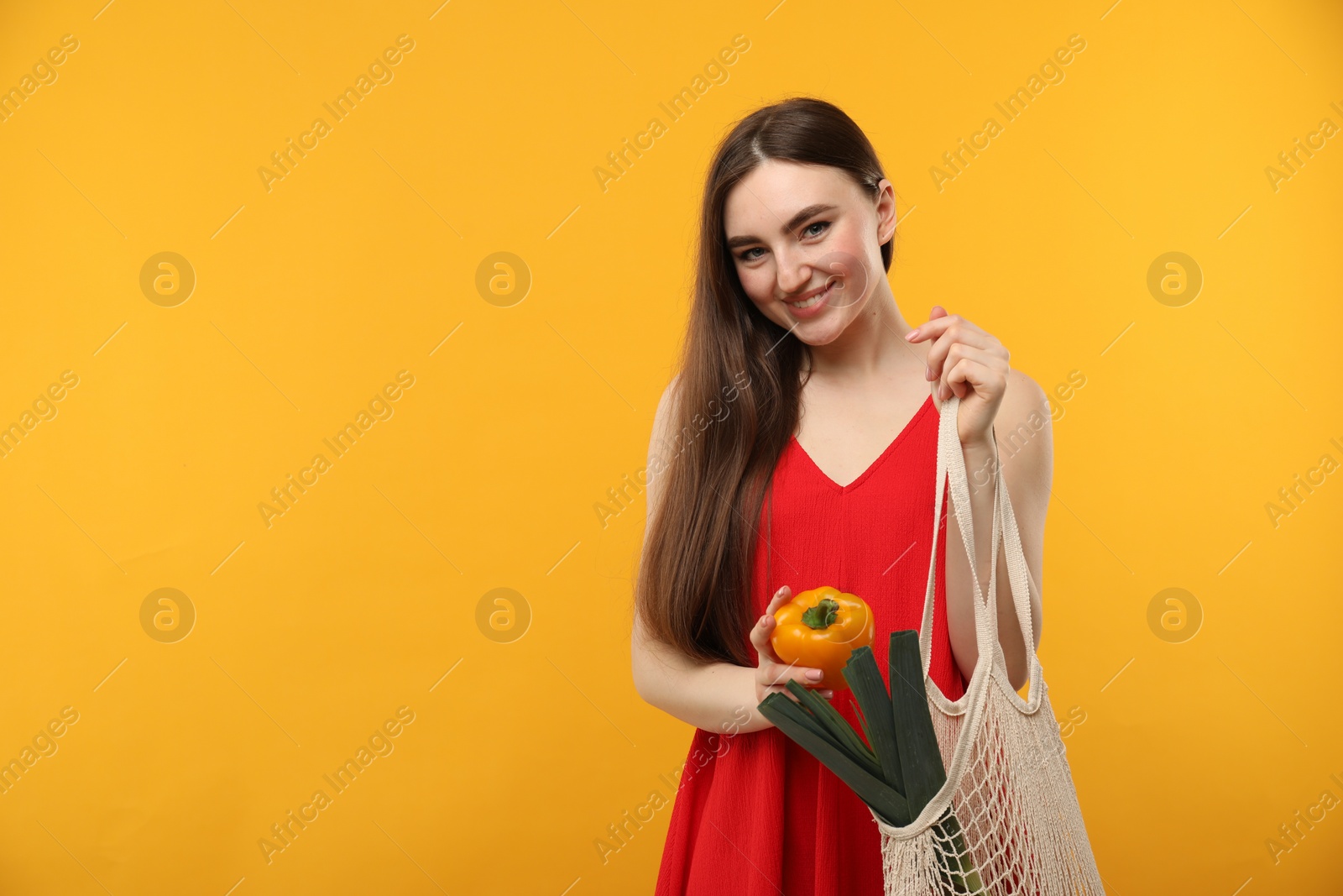 Photo of Woman with string bag of fresh vegetables on orange background, space for text